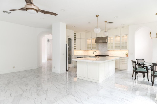 kitchen with stainless steel refrigerator, white cabinetry, tasteful backsplash, a kitchen island with sink, and pendant lighting