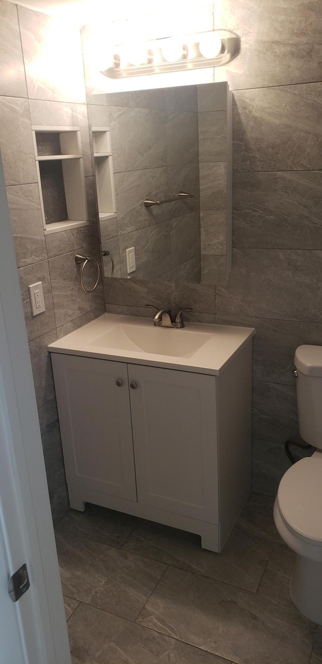 bathroom with tile walls, vanity, and toilet