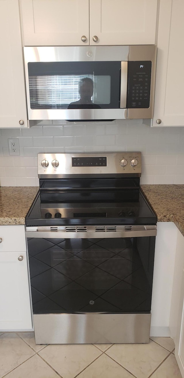 kitchen featuring dark stone counters, appliances with stainless steel finishes, light tile patterned floors, and white cabinets