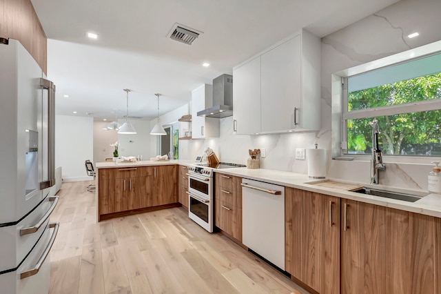 kitchen with wall chimney range hood, white cabinetry, light wood-type flooring, white appliances, and decorative light fixtures