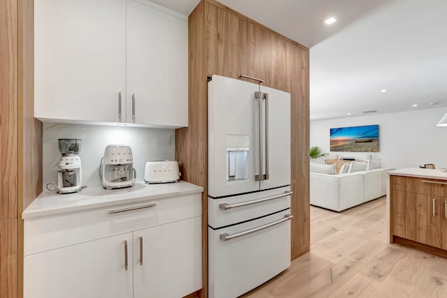 kitchen with white cabinets, light wood-type flooring, high end white fridge, and light stone countertops