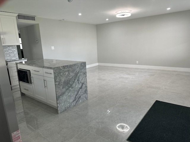 kitchen with white cabinets, backsplash, a kitchen island, and light stone countertops