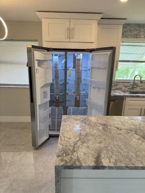 kitchen with white cabinets, backsplash, light stone countertops, and sink