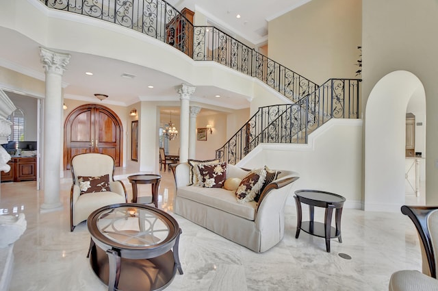 living room with a high ceiling, decorative columns, an inviting chandelier, and ornamental molding