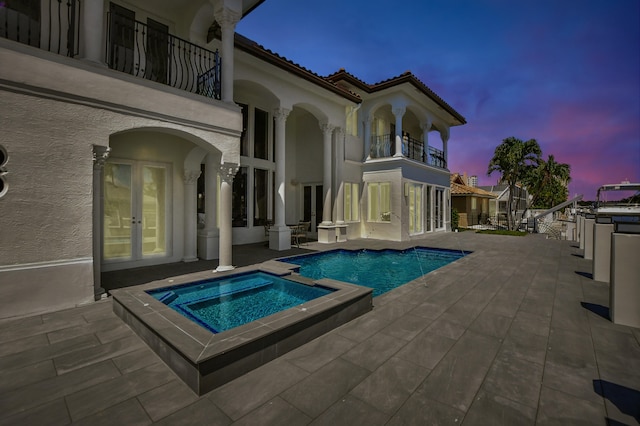 pool at dusk featuring a patio, french doors, and an in ground hot tub