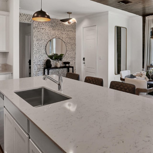 kitchen featuring crown molding, sink, hanging light fixtures, white cabinetry, and light stone counters