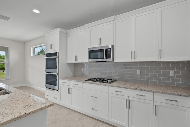 kitchen with tasteful backsplash, appliances with stainless steel finishes, light tile patterned flooring, white cabinets, and light stone counters