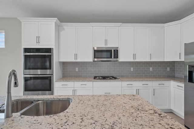 kitchen with decorative backsplash, white cabinetry, stainless steel appliances, and sink