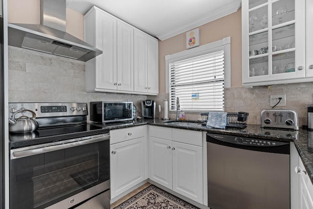 kitchen with dark stone counters, white cabinetry, wall chimney range hood, appliances with stainless steel finishes, and sink