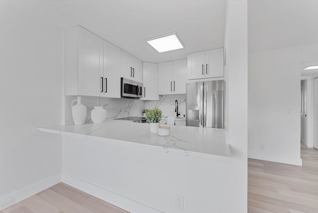 kitchen featuring tasteful backsplash, white cabinetry, appliances with stainless steel finishes, and light hardwood / wood-style flooring