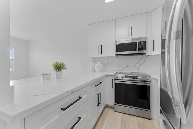 kitchen featuring stainless steel appliances, white cabinetry, kitchen peninsula, light stone counters, and backsplash