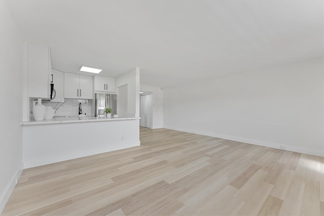 kitchen with white cabinets, stainless steel refrigerator with ice dispenser, light wood-type flooring, and kitchen peninsula