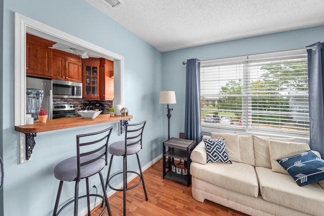 kitchen with a kitchen bar, light hardwood / wood-style floors, a textured ceiling, backsplash, and appliances with stainless steel finishes