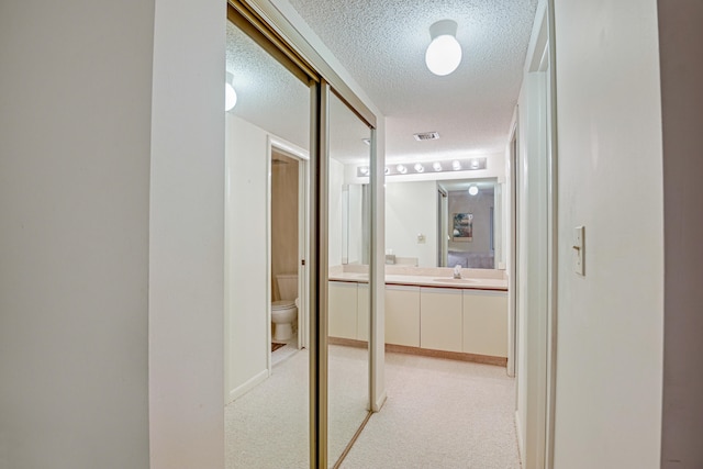 hall with light carpet, a textured ceiling, and sink