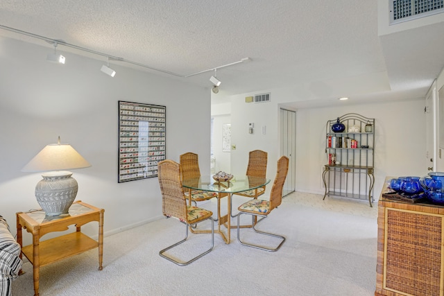 dining space with light colored carpet, a textured ceiling, and track lighting