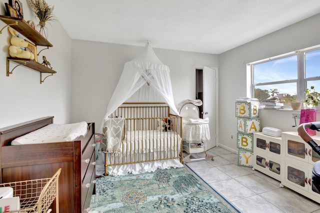 bedroom featuring a textured ceiling, light tile patterned floors, and a nursery area