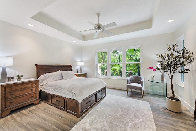 bedroom featuring light hardwood / wood-style flooring, ceiling fan, and a raised ceiling