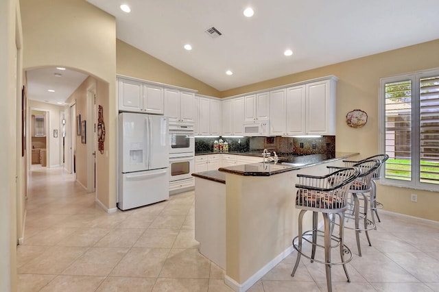 kitchen featuring white cabinetry, kitchen peninsula, a kitchen bar, white appliances, and vaulted ceiling