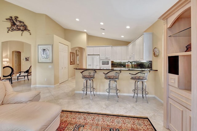 kitchen with white appliances, a breakfast bar area, white cabinetry, and kitchen peninsula