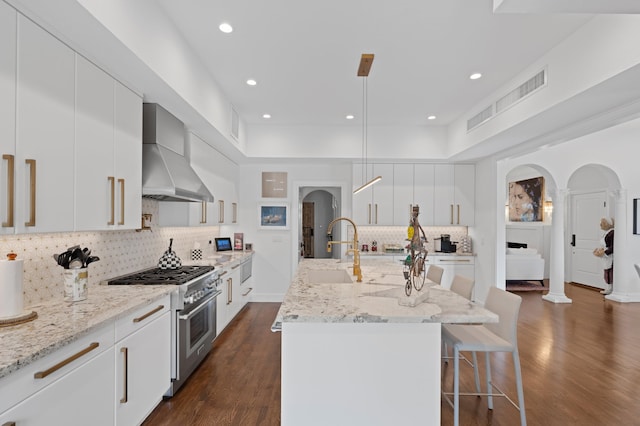 kitchen with white cabinetry, wall chimney exhaust hood, a center island with sink, and double oven range