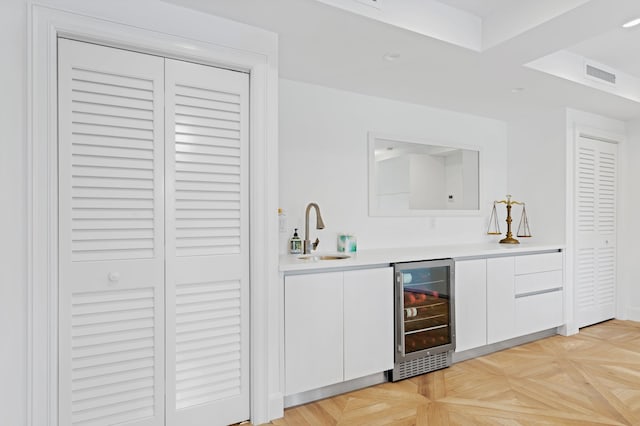 bar with white cabinetry, light parquet flooring, sink, and beverage cooler