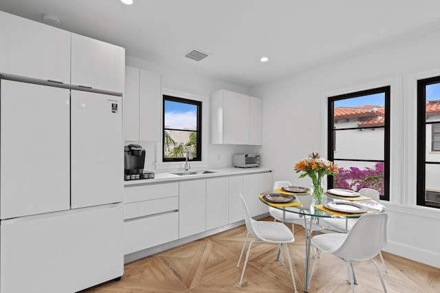 kitchen with light parquet floors, white cabinetry, white fridge, and sink