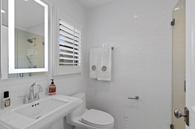 bathroom featuring tasteful backsplash, a tile shower, tile walls, toilet, and sink