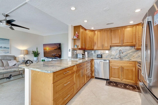 kitchen featuring light stone counters, appliances with stainless steel finishes, a textured ceiling, sink, and kitchen peninsula