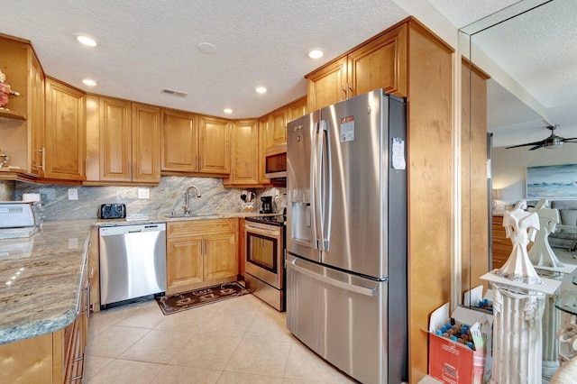 kitchen with stainless steel appliances, sink, light stone counters, tasteful backsplash, and ceiling fan