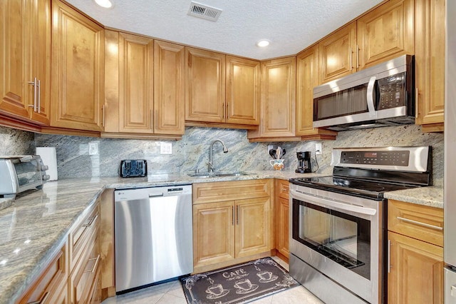 kitchen with backsplash, sink, light stone counters, and stainless steel appliances