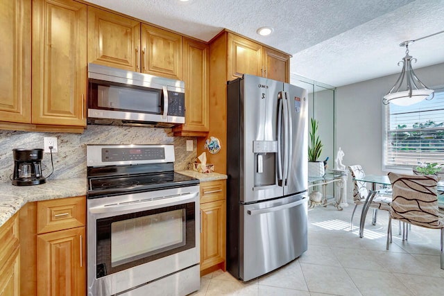 kitchen with appliances with stainless steel finishes, light tile patterned flooring, light stone counters, and backsplash