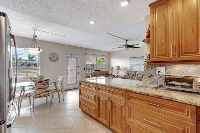 kitchen with ceiling fan, light stone countertops, stainless steel refrigerator, and pendant lighting