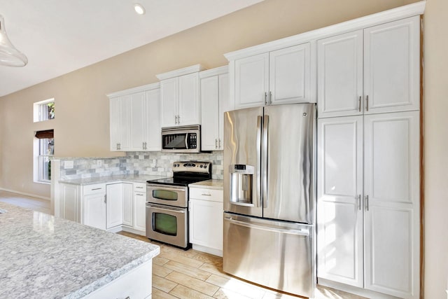 kitchen with white cabinets, light wood-type flooring, appliances with stainless steel finishes, tasteful backsplash, and light stone counters