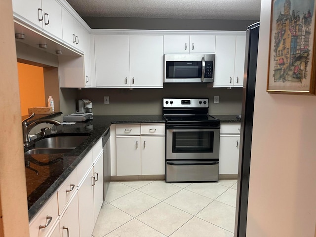 kitchen featuring stainless steel appliances, dark stone countertops, white cabinets, and sink