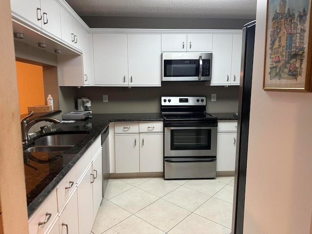 kitchen with stainless steel appliances, dark stone countertops, white cabinetry, and sink