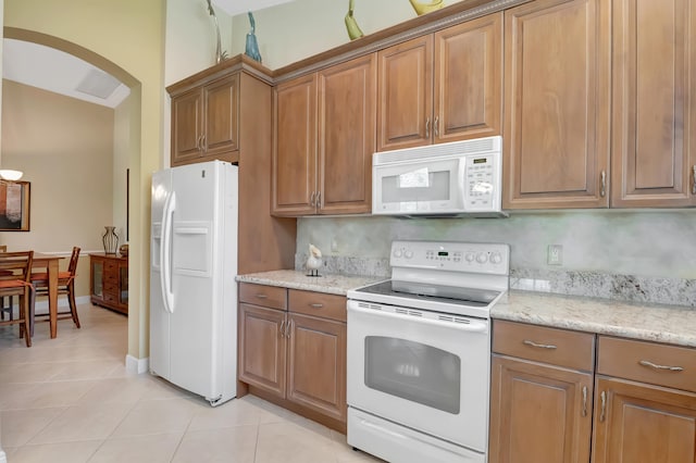 kitchen featuring tasteful backsplash, light stone countertops, light tile patterned floors, and white appliances