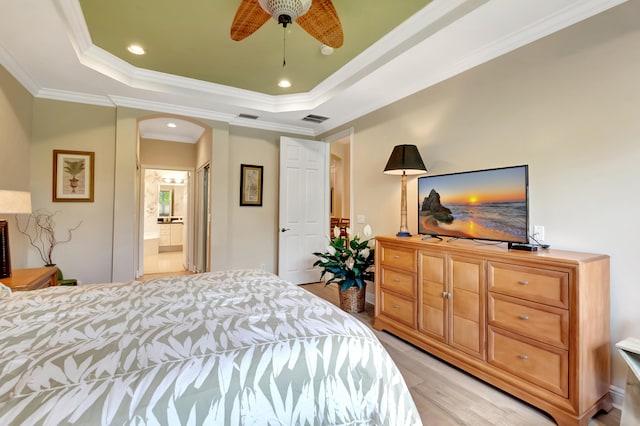 bedroom with crown molding, ceiling fan, connected bathroom, a tray ceiling, and light hardwood / wood-style floors