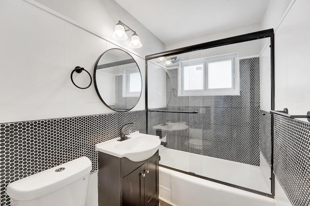 full bathroom with bath / shower combo with glass door, vanity, toilet, and tile walls