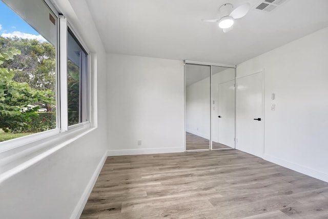 unfurnished bedroom with a closet, multiple windows, ceiling fan, and light hardwood / wood-style flooring