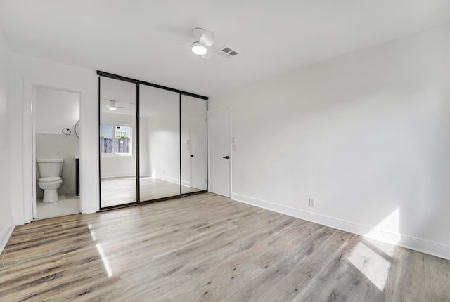 unfurnished bedroom featuring light wood-type flooring, ensuite bath, ceiling fan, and a closet