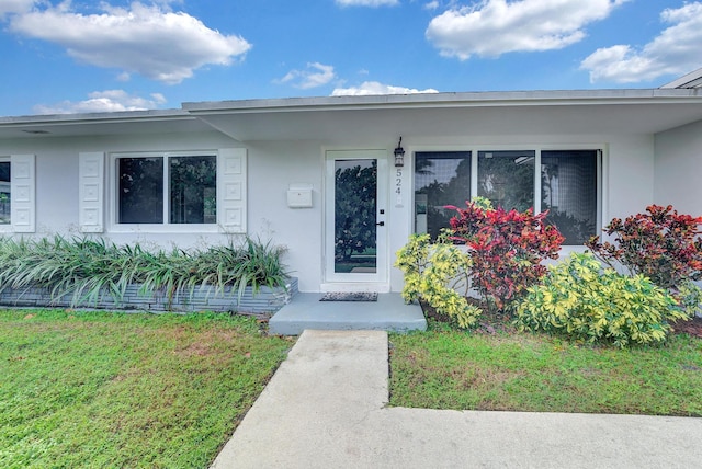 524 Lighthouse Dr, North Palm Beach, FL 33408 - doorway to property featuring stucco siding and a lawn