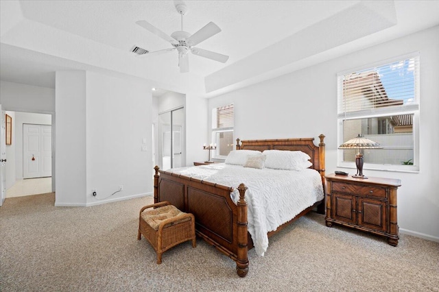 carpeted bedroom featuring a raised ceiling, ceiling fan, and a closet