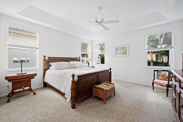 carpeted bedroom with ceiling fan, multiple windows, and a tray ceiling