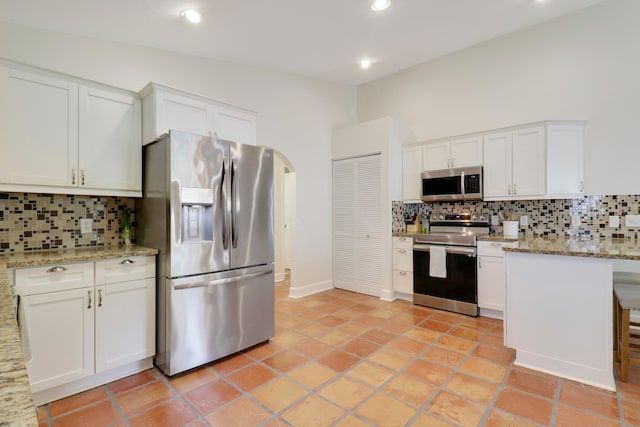 kitchen with tasteful backsplash, stainless steel appliances, a kitchen bar, light stone countertops, and white cabinets