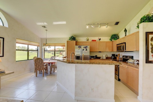 kitchen featuring appliances with stainless steel finishes, vaulted ceiling, pendant lighting, dark stone countertops, and an island with sink