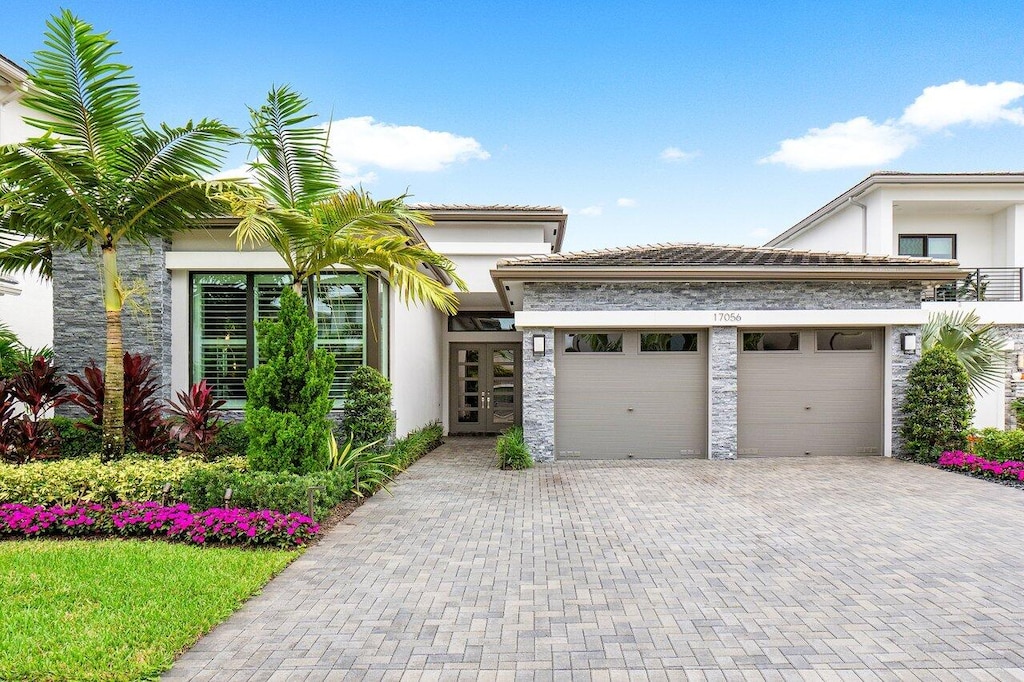 17056 Cappuccino Way, Boca Raton, FL 33496 - view of front of home with french doors, a garage, stucco siding, decorative driveway, and stone siding