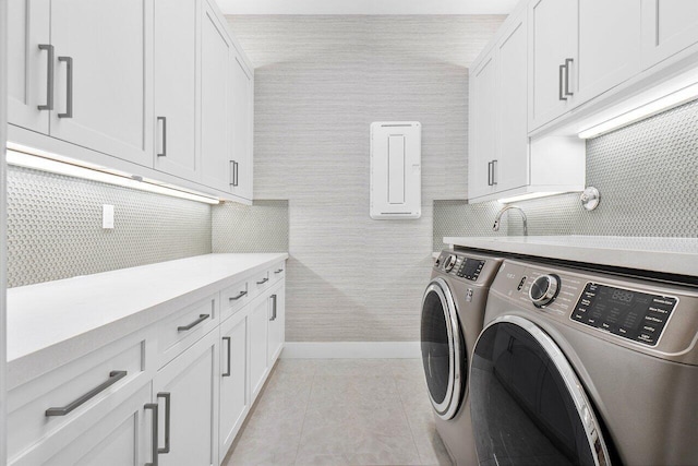 laundry room featuring washing machine and dryer, light tile patterned flooring, and cabinets