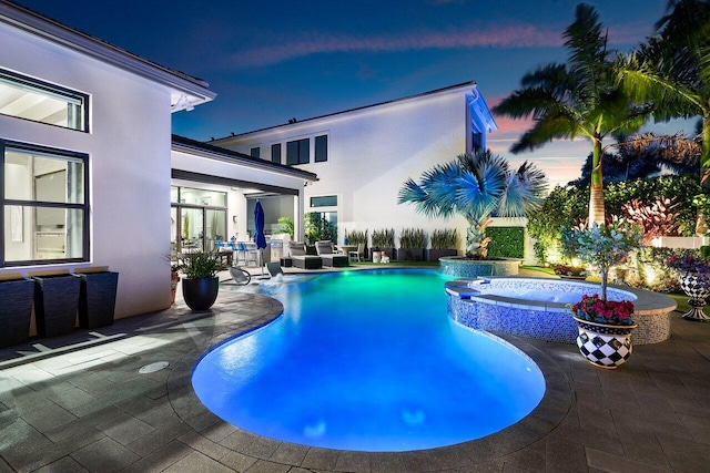 pool at dusk featuring an in ground hot tub and a patio