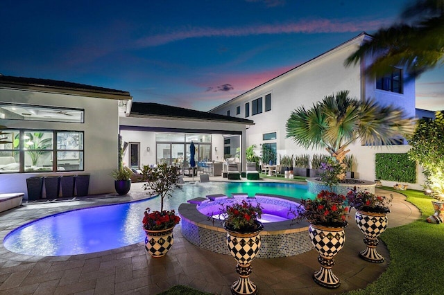 pool at dusk featuring a patio area and an in ground hot tub