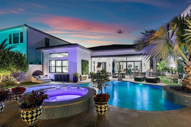 pool at dusk with a patio area and an in ground hot tub